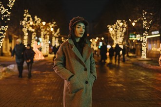 Young woman wearing coat on street at night with fairy lights