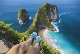 Legs of woman sitting above Kelingking Beach in Nusa Penida, Indonesia