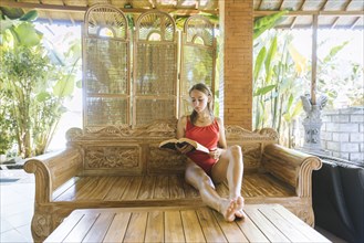 Woman wearing swimsuit reading book on wooden sofa