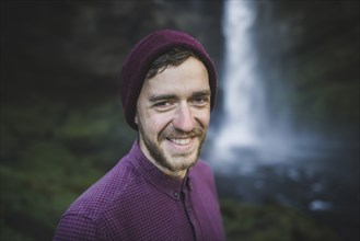 Portrait of smiling young man by Kvernufoss waterfall in Iceland