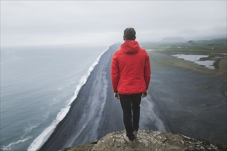 Man wearing red coat above beach in Vik, Iceland