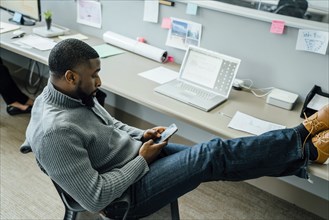 Man with his feet up using smart phone in office