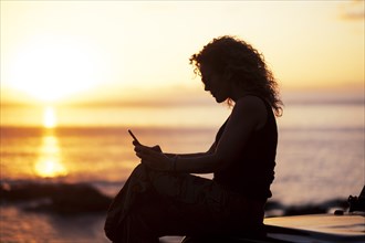Woman using smart phone by beach at sunset