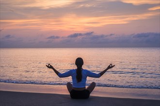 Woman practicing yoga on beach at sunset