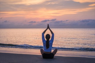 Woman practicing yoga on beach at sunset