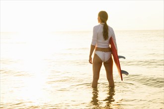 Woman holding surfboard in sea at sunset