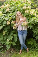 Smiling young woman holding smoothie by flowers