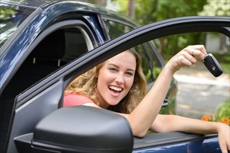 Smiling young woman in car holding car keys