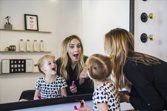 Mother and daughter applying lipstick in mirror