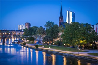 Church and office towers by river at sunset in Frankfurt