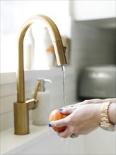 Hands of woman washing apple in kitchen sink