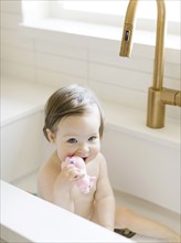 Baby girl biting pig toy while bathing in kitchen sink