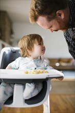 Father looking at baby girl in high chair