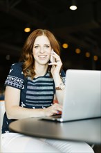 Smiling mid adult woman using smart phone and laptop