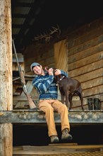 Man petting chocolate Labrador on porch of log cabin