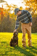 Man petting chocolate Labrador in field during autumn