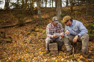Men with fishing rods and box sitting on logs during autumn