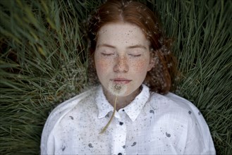 Teenage girl lying down with dandelion seedhead