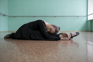 Ballet dancer wearing black dress stretching in studio