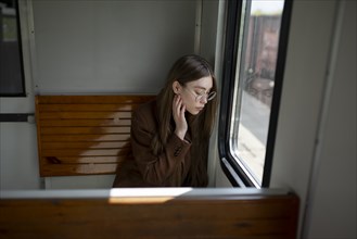 Young woman wearing glasses by window on train