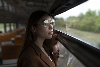 Young woman wearing glasses looking out of train window