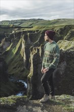 Young man standing on cliff above canyon in Kirkjubµjarklaustur