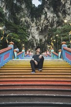 Young man sitting on colorful staircase by cliffs in Kuala Lumpur