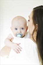 Baby boy using pacifier looking over his mother's shoulder