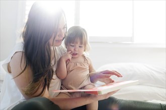 Woman reading book to her daughter on bed