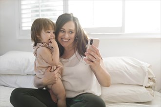 Mother and daughter taking selfie on bed
