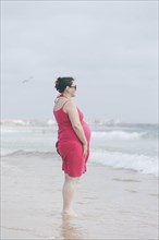 Pregnant woman wearing pink dress on beach