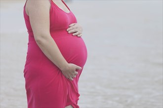 Pregnant woman wearing pink dress on beach