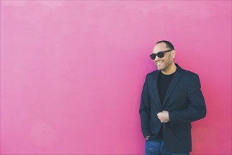 Smiling man wearing sunglasses and blazer by pink wall