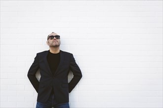 Man wearing sunglasses and blazer by white wall