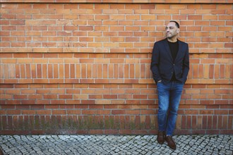 Man wearing blazer and jeans by brick wall