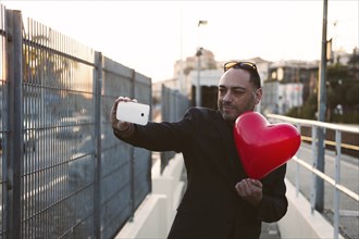 Man taking selfie with red heart shaped balloon