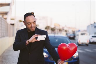 Man photographing red heart shaped balloon