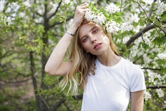 Blond haired young woman among white blossoms