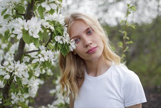 Blond haired young woman among white blossoms