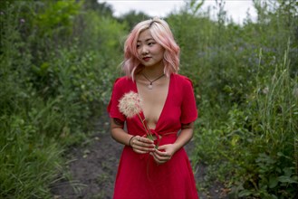 Young woman wearing red dress holding seed head