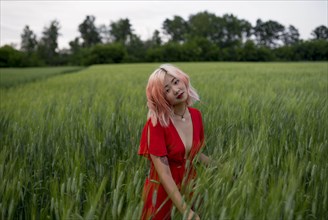 Woman with pink hair wearing red dress in wheat field