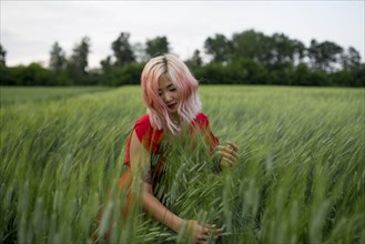 Woman with pink hair wearing red dress in wheat field