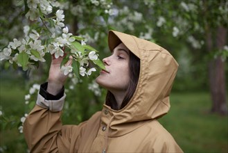 Young woman wearing brown raincoat sniffing flower