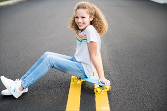 Girl sitting on skateboard on road