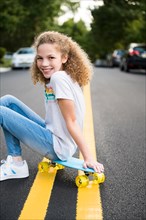 Girl sitting on skateboard on road