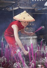 Woman lighting incense in temple in Lijang, Shangri-La Region, Yunnan Province, China