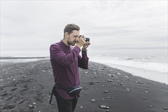 Man taking photograph on beach in Iceland