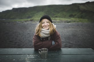 Young woman wearing warm clothing at picnic table on beach