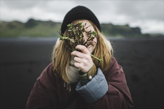 Woman holding plants over her face on beach