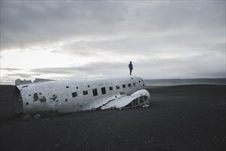 Man standing on abandoned airplane in black sand desert